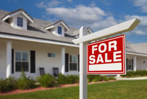 A red FOR SALE sign in front of a white house. Creator: Feverpitched  |  Credit: Getty Images